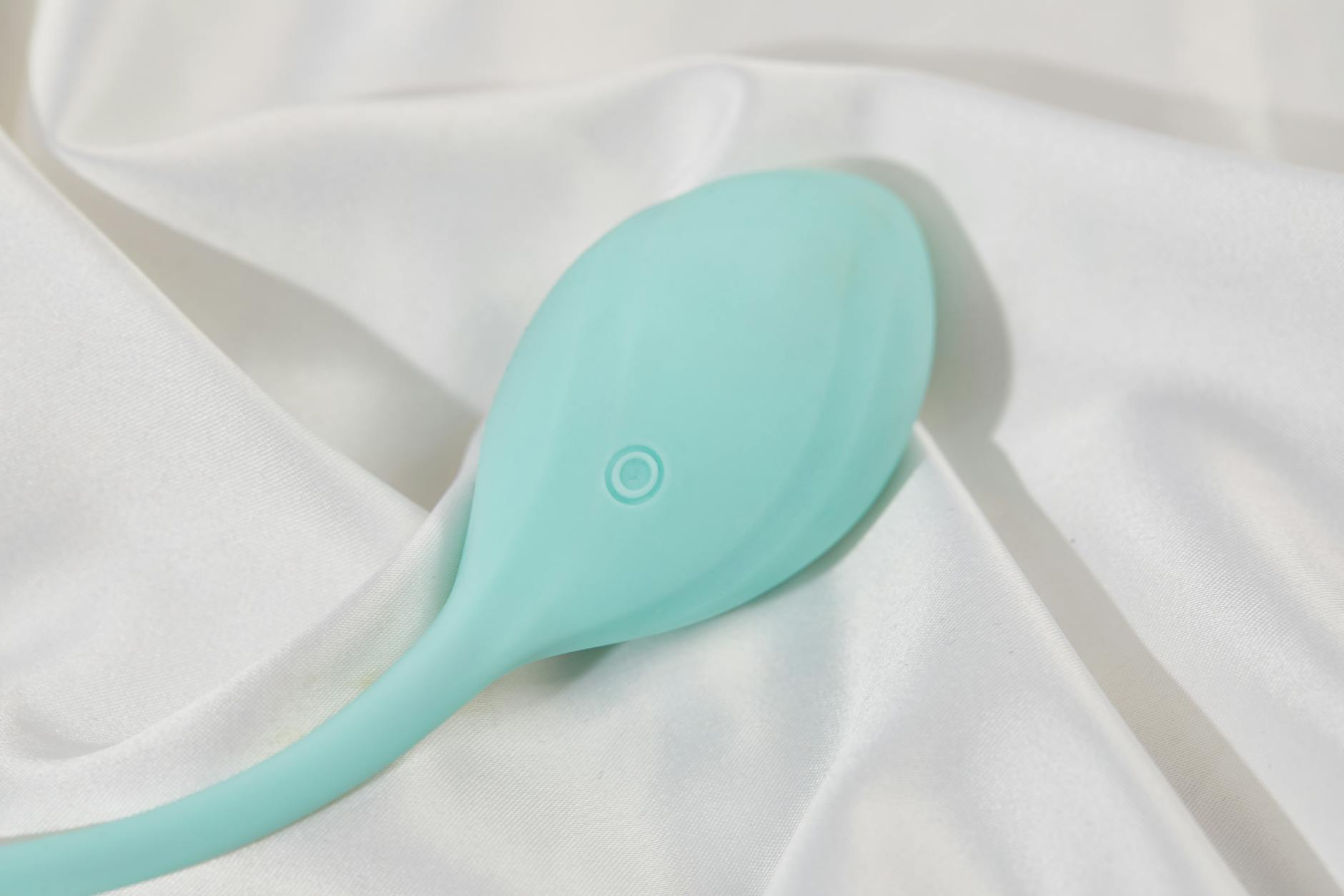 A sleek teal lemon clitoral vibrator on soft white silk, illustrating how natural lubrication interacts with suction technology