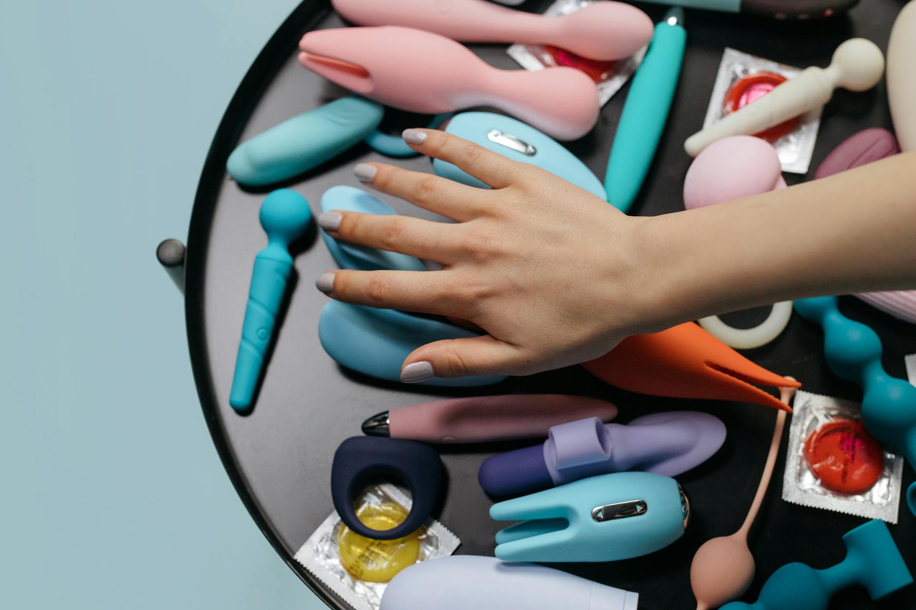 A hand holding a blue silicone vibrator against a purple background