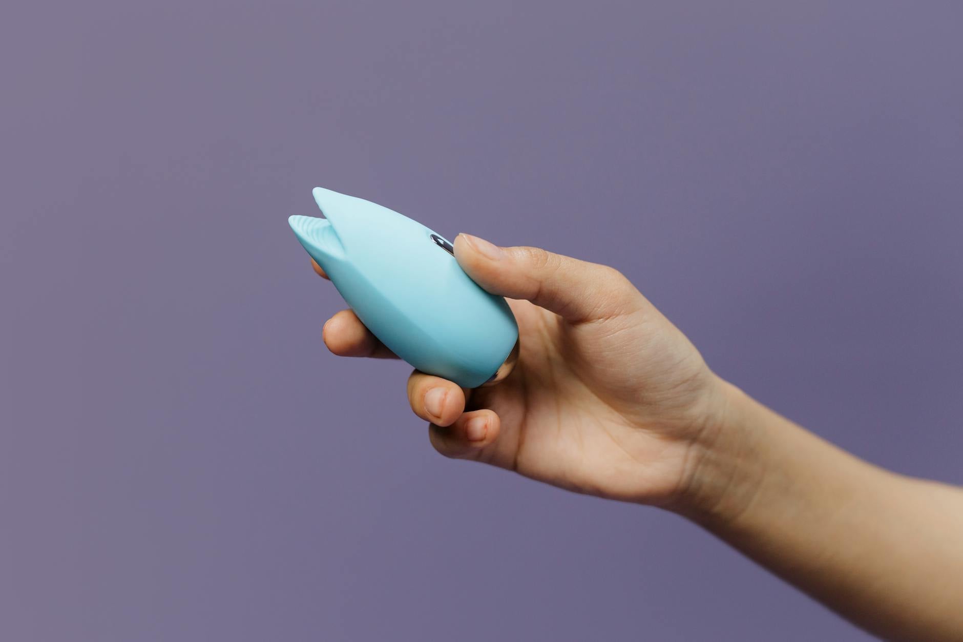 A hand holding a blue lemon vibrator against a solid purple background, representing exploration and self-discovery