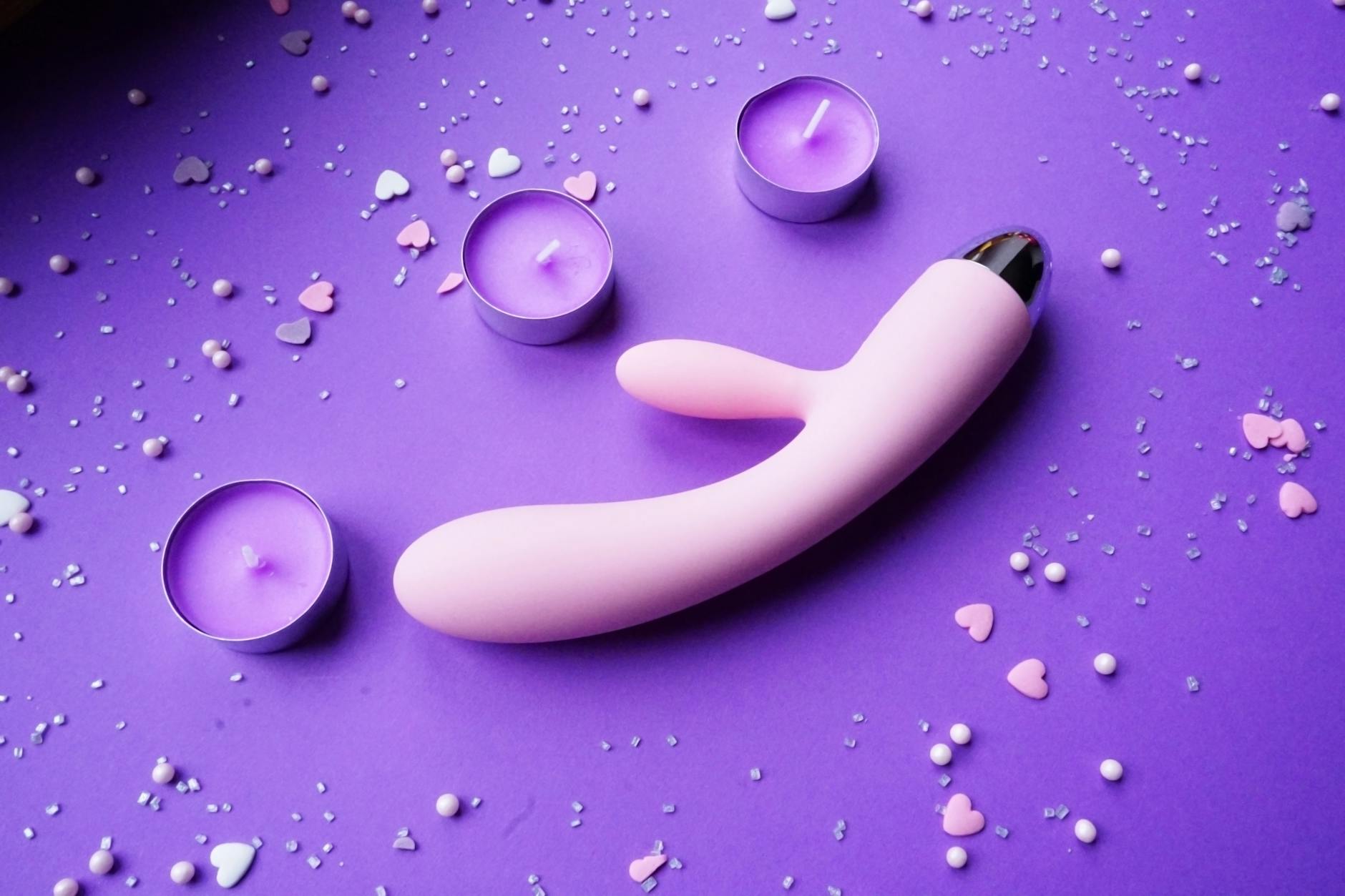 Pink vibrator surrounded by heart confetti and candles on a romantic purple background